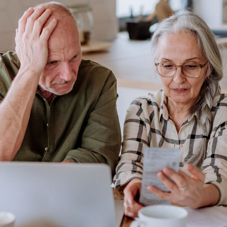 elderly couple appearing stressed over receipt and laptop