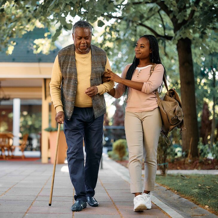 young woman helping older man walk with a cane