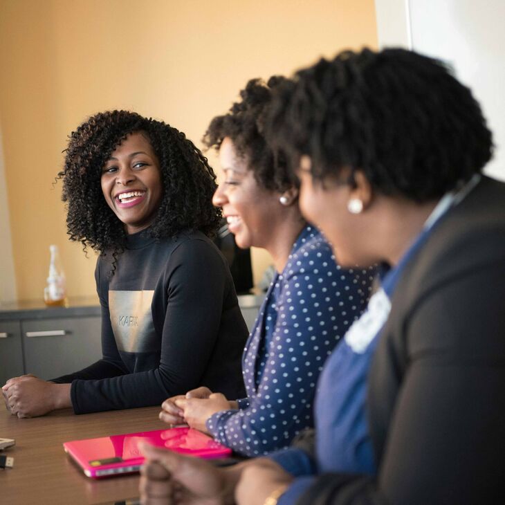 smiling woman leaning on desk while talking to two other women