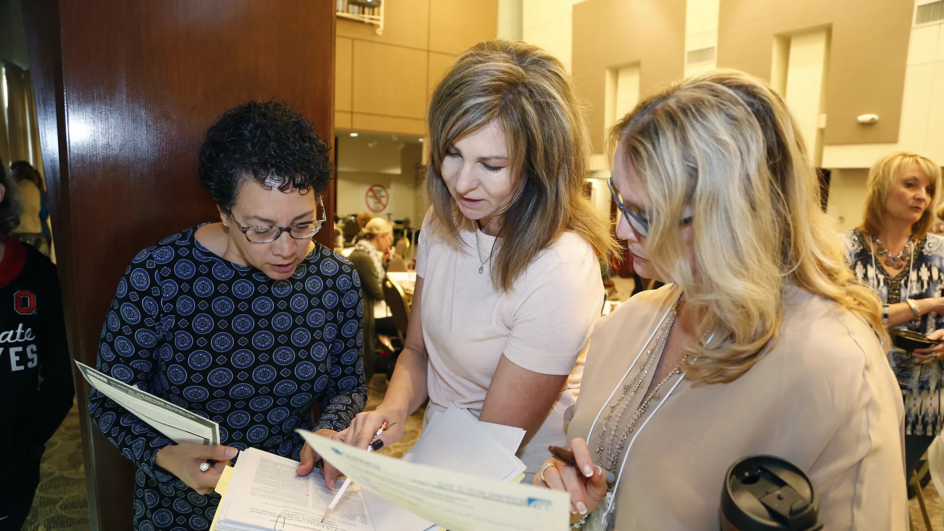 Three women at a conference looking at a sheet of paper in a binder.