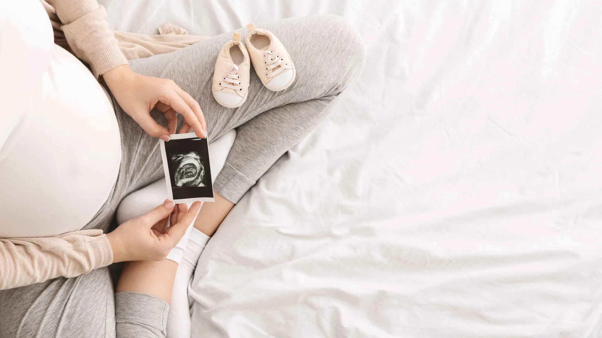 pregnant woman looking at ultrasound in her lap with a pair of baby shoes on her leg
