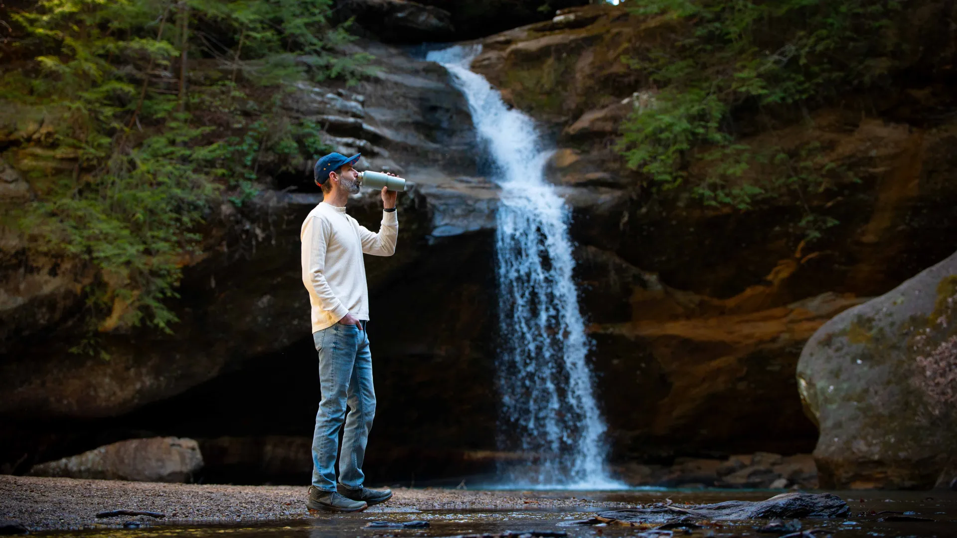 Man drinking water in front of a waterfall