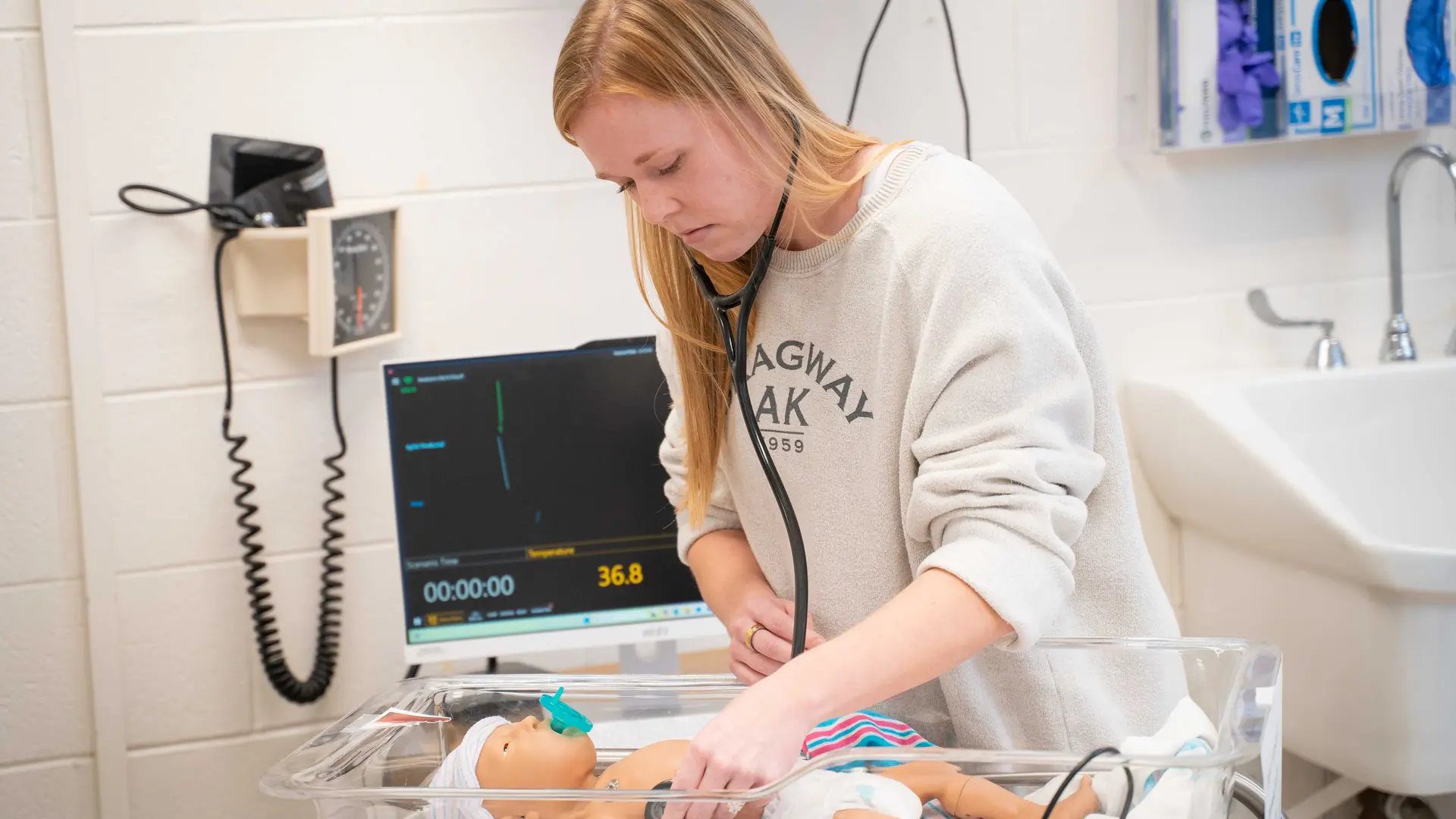 student uses stethoscope on nursing simulation baby during lab