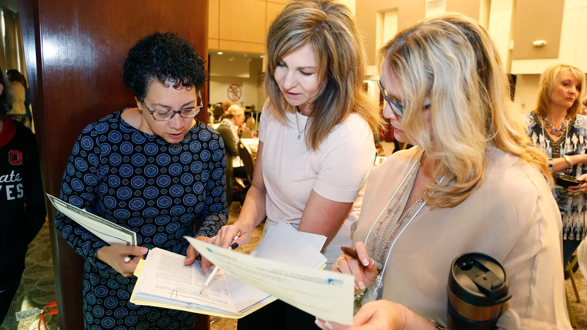 Three women at a conference looking at a sheet of paper in a binder.