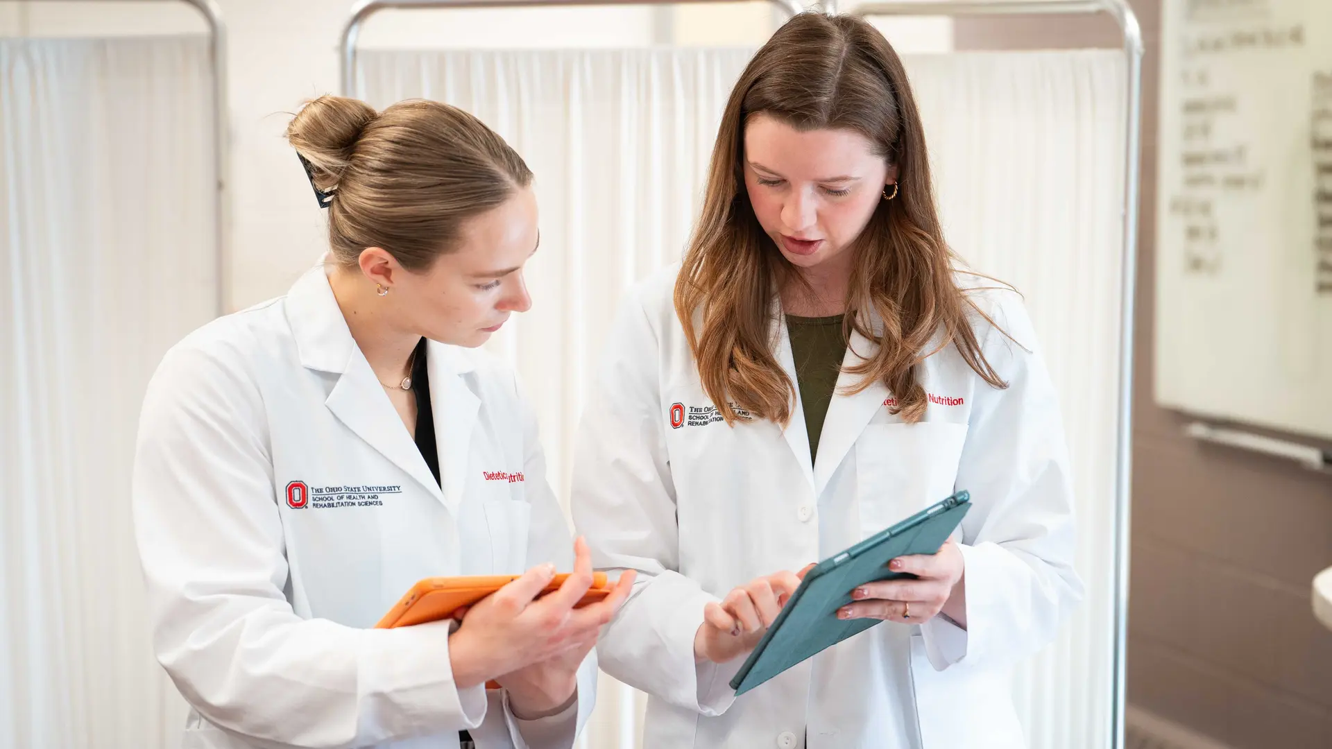 nurses in white scrubs discuss a patient's chart