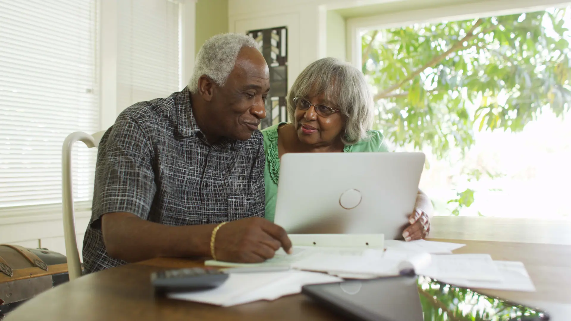 Elderly couple sitting at a table, using laptop computer